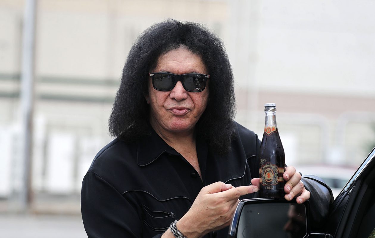 Gene Simmons holding and pointing towards bottle of soda